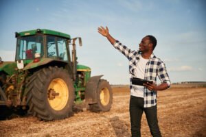 Standing, holding tablet. Beautiful African American man is in the agricultural field.